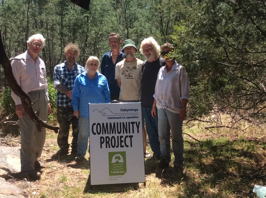 Seven members of the Dabyminga Catchment Co-operative standing in the bush behind a sign reading Community Project.